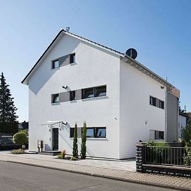 Modernes weißes Wohnhaus mit Satteldach und mehreren schmalen Fenstern an einer ruhigen Straße.