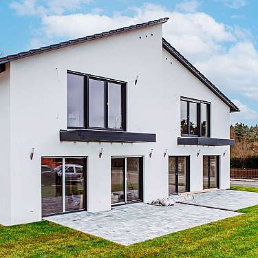 Weiße moderne Doppelhaushälfte mit großen Fenstern und Terrasse auf grünem Rasen.